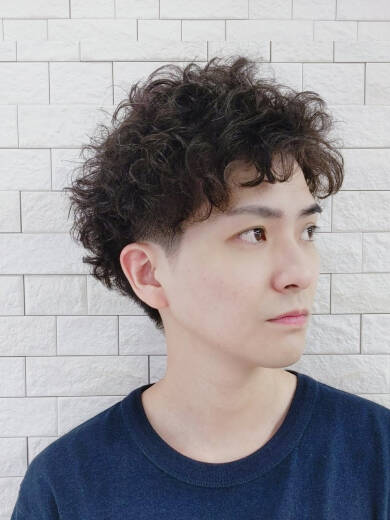 カールのかかったショートヘアの男性が横を向いている写真。