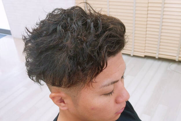 パーマがかかった男性のヘアスタイル、トップにボリュームを持たせた仕上がり